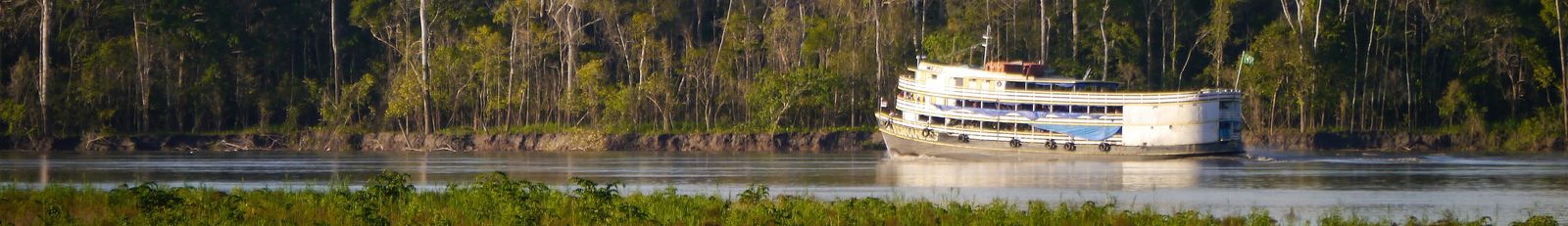 A wooden riverboat navigating a wide, calm stretch of the Amazon River beneath an overcast sky