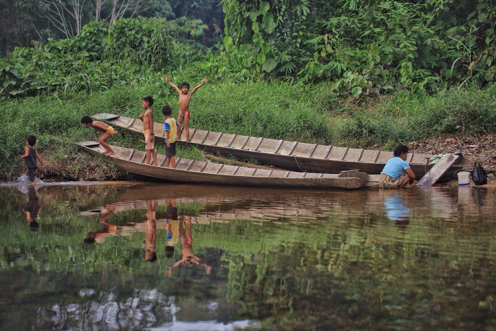 A dugout canoe on a calm rainforest river with people boarding at the bank