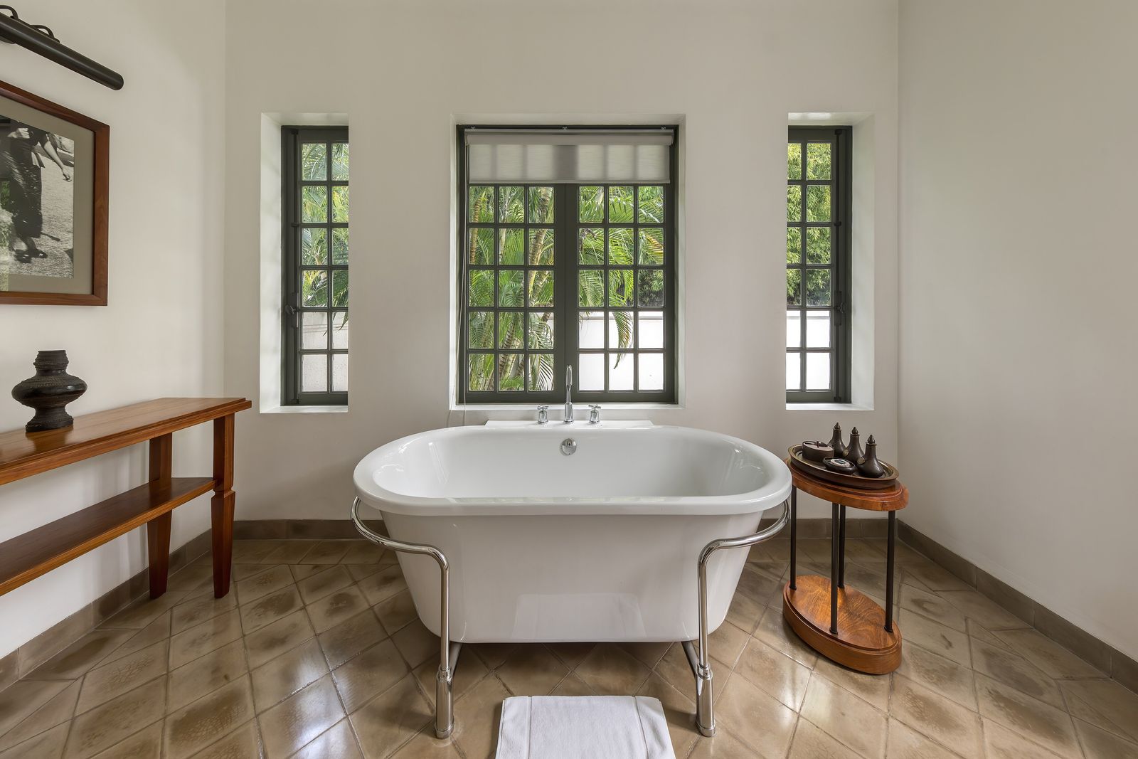 A freestanding white bathtub beside large windows opening onto tropical greenery