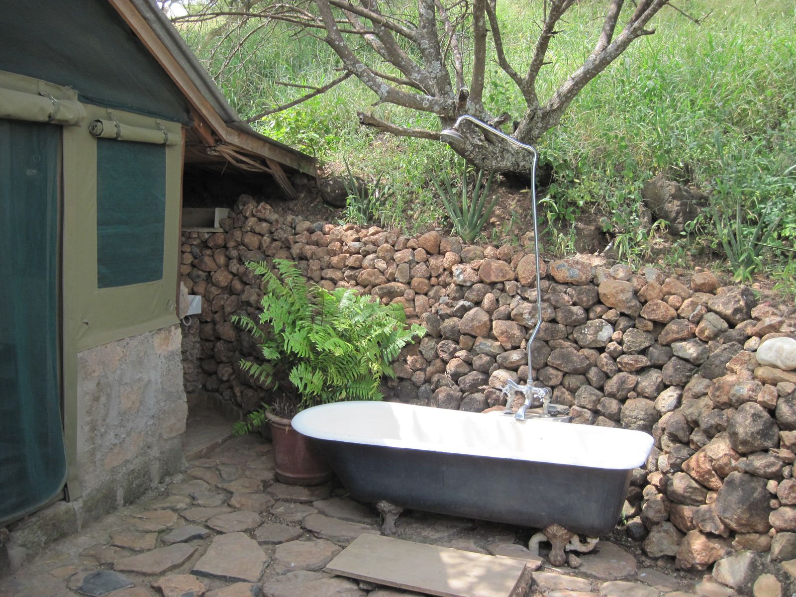 An outdoor clawfoot bathtub and shower in a private stone-walled garden enclosure open to the sky