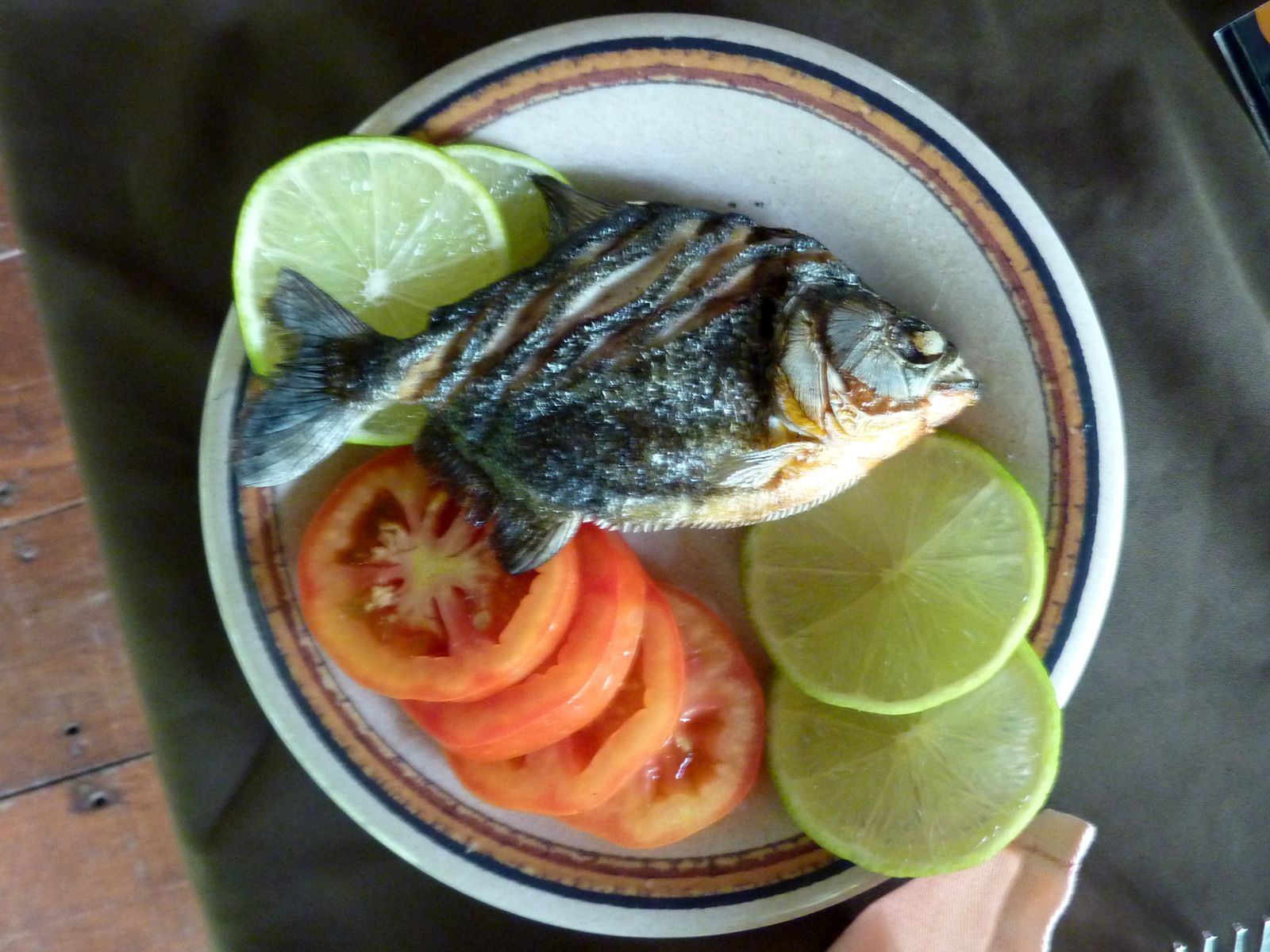A whole grilled piranha served on a plate with slices of lime and tomato